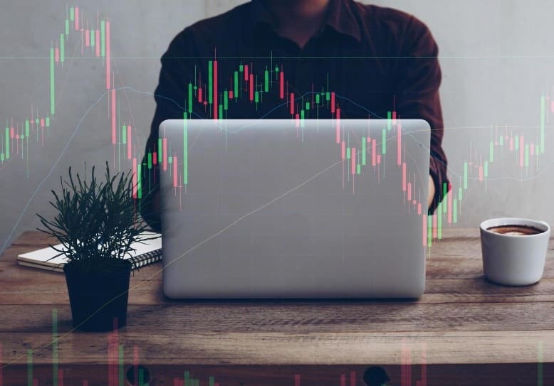 người đàn ông ngồi sau máy tính xách tay với biểu đồ giao dịch phủ lên