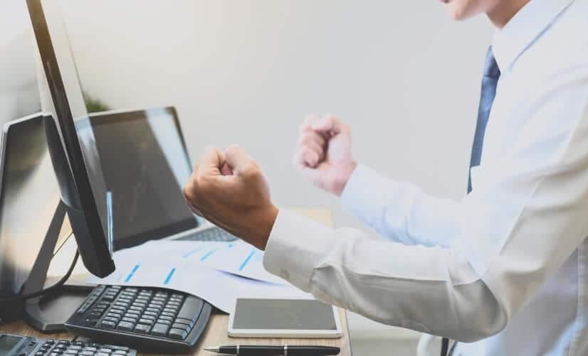 man shaking fists in front of pc and tablet showing trading chart