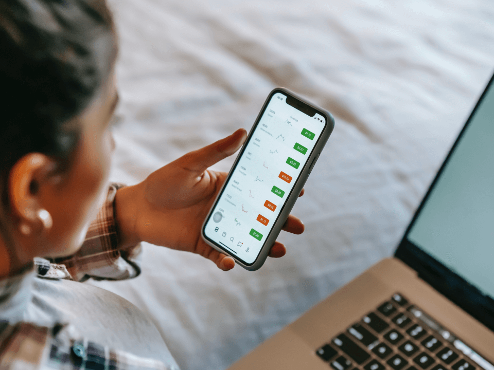 A Person Checking A Trade On Their Smartphone Sitting On A Bed